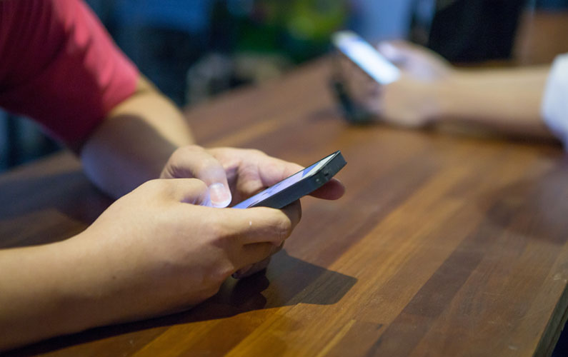 people at wooden table texting on their phones