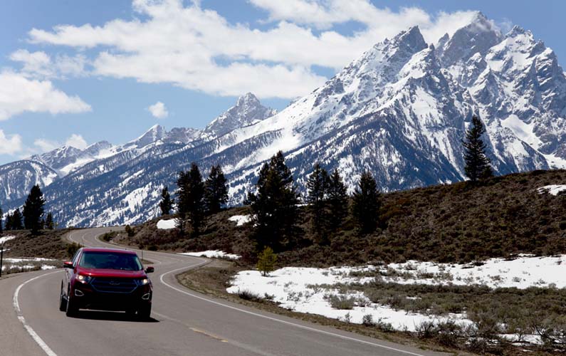 grand-teton-national-park-tetons-snow-covered-in-may-red-car-driving-on-road