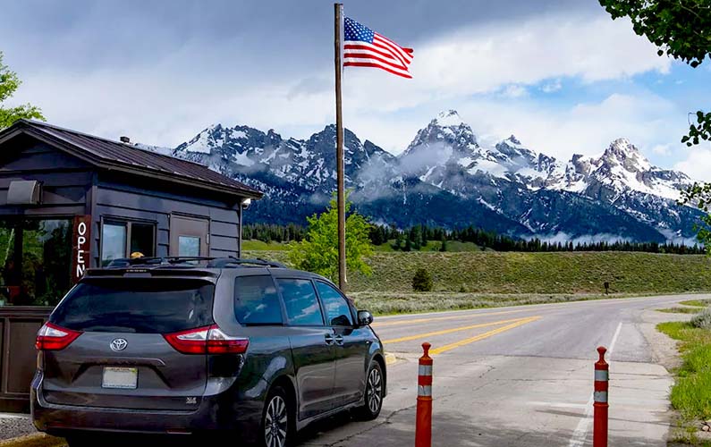 grand-teton-national-park-entrance-at-moose-wy-gate-open-sign-american-flag-tetons-background